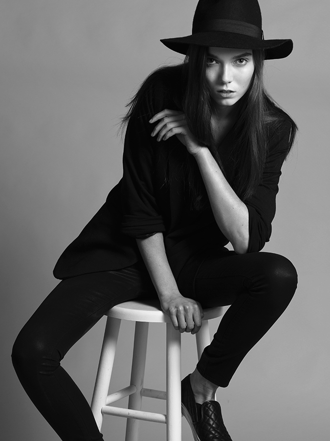 Next model Briley Jones sitting on a white modeling stool in a black suit and hat photographed in black and white by Joshua Pyles