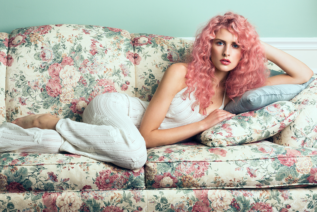 Ford model Jordan Strange posing on floral couch with curly pink hair wearing a white knit For Love and Lemons jumpsuit photographed by Joshua Pyles