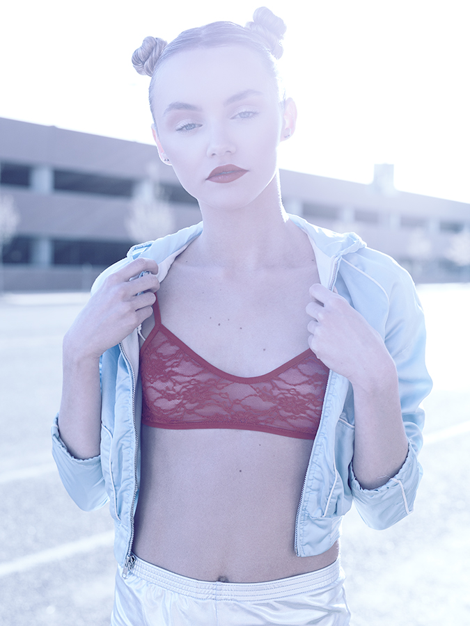 Fashion image of model Kateri Dion on the street in braided pigtails wearing a sheer lace red bralet, metallic blue vintage 80s jacket, and silver metallic disco shorts photographed by Joshua Pyles