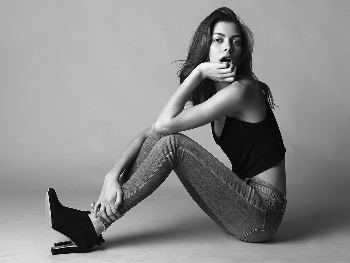 Model Kayla Travers poses with hand to lips on studio floor in jeans and tank-top photographed in black and white by Joshua Pyles