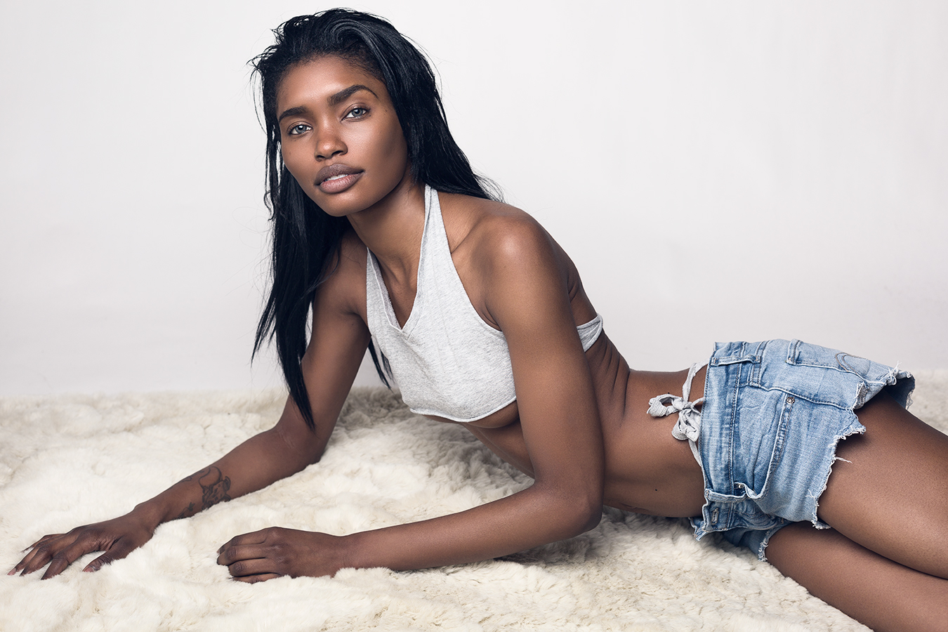 Model Tosh Bellington in cropped grey t-shirt and cut-off shorts recling on soft carpet photographed by Joshua Pyles